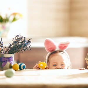 Beautiful child painting eggs. Happy family preparing for Easter. Cute little girl is wearing bunny ears.